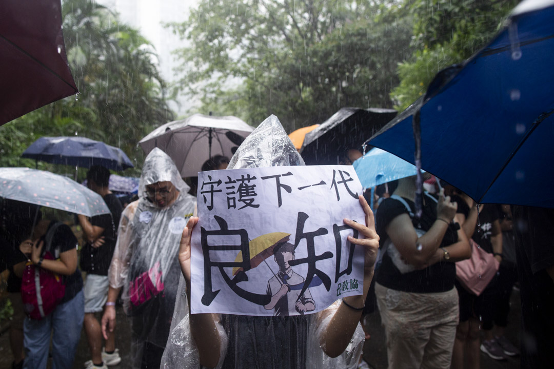 2019年8月17日，有教师发起“守护下一代，为良知发声”的游行，期间大雨滂沱，参加者身上贴上“我是香港教师”的贴纸，又手持“守护下一代良知”、“凭老师守护”的标语。 摄：林振东/端传媒 