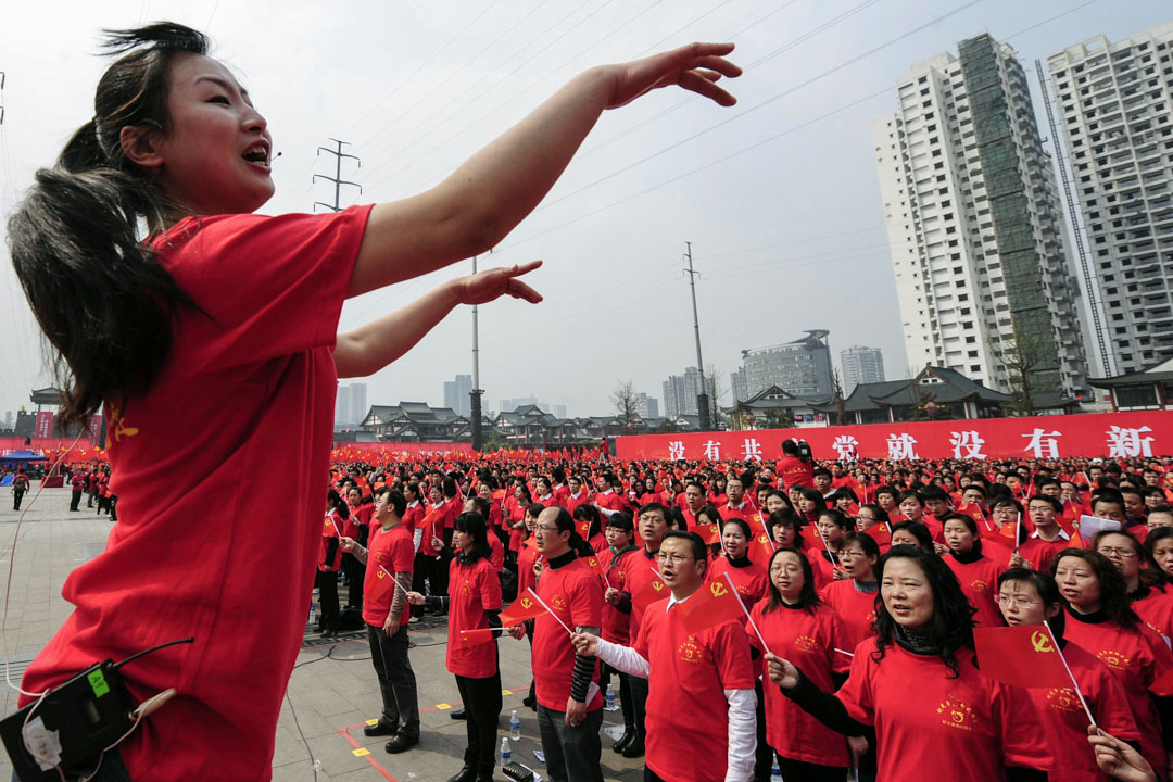 2011年3月28日，重庆市的一个广场上，为庆祝即将到来的中共成立90周年活动，一名指挥带领群众唱革命歌曲。