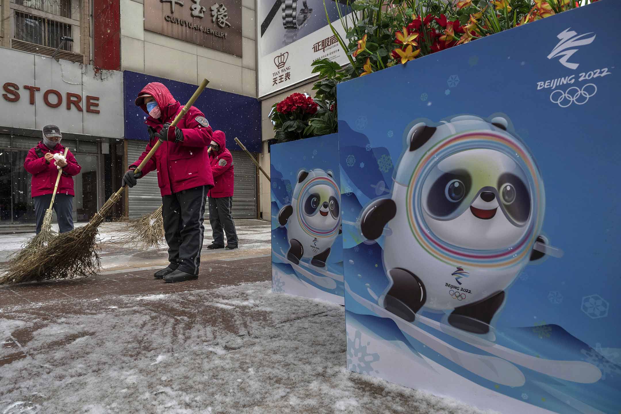 2022年1月20日北京，志愿者在北京冬奥会和残奥会海报旁边扫雪，海报展示了吉祥物“冰墩墩”。