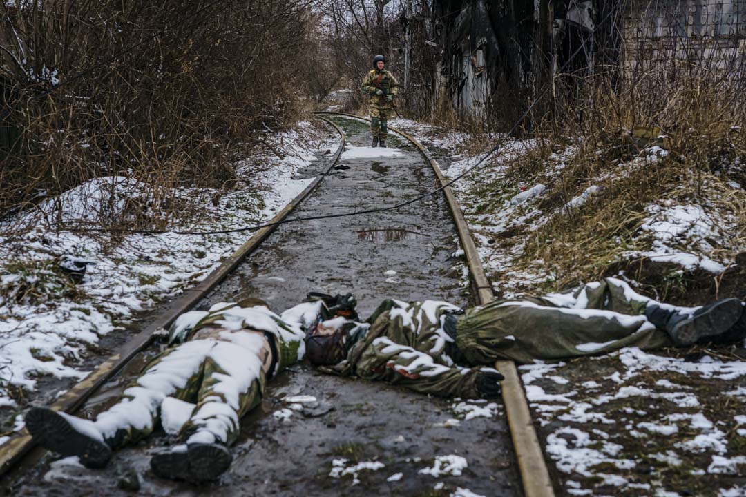 2022年3月1日，乌克兰伊尔平郊区，一名乌克兰士兵从铁路上回来，经过俄罗斯士兵的尸体，在那里曾与俄军发生激战。摄：Marcus Yam / Los Angeles Times 