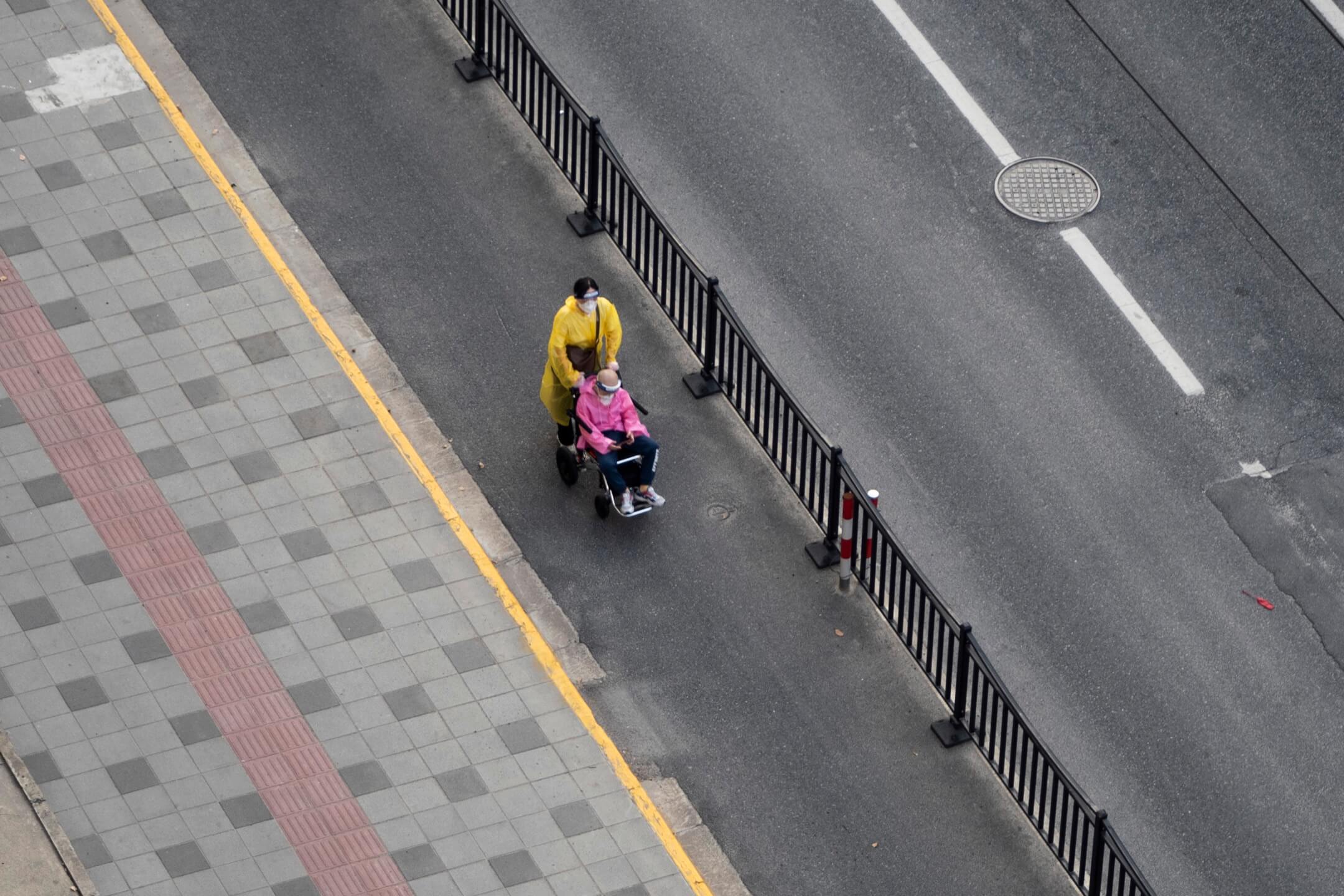 2022年4月12日，上海封城，一名居民推著一名坐輪椅的老人家在街上行走。