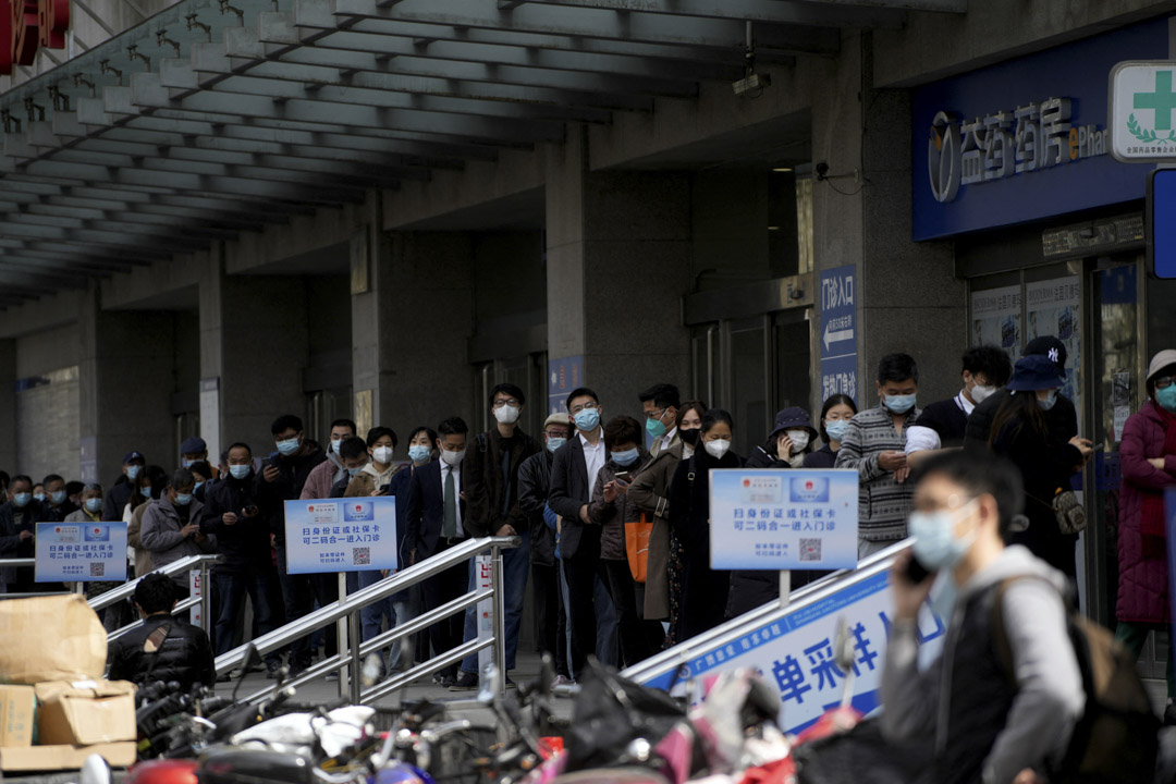 2022年3月30日，上海爆发COVID-19后，戴著口罩的人在医院外排队接受核酸检测。