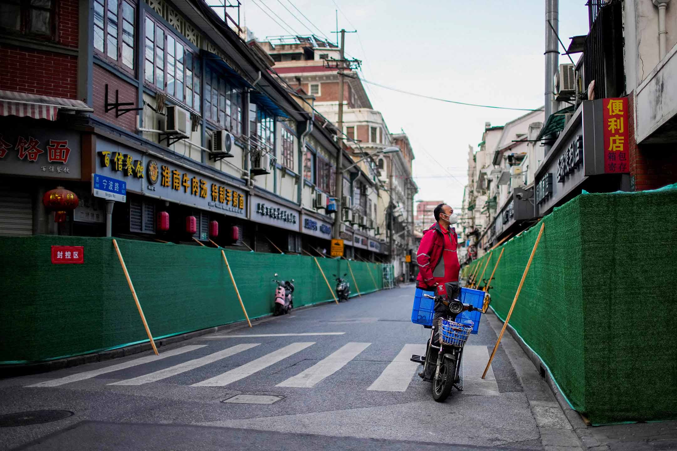 2022年5月9日，上海，疫情期间，一名站在机车上的送货员在封锁的住宅区探看。