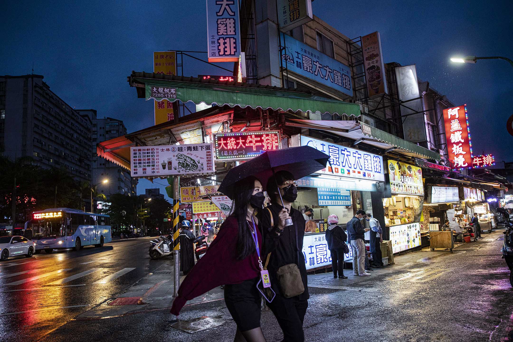 2022年4月21日，台北士林夜市，游人走过夜市上的食店。