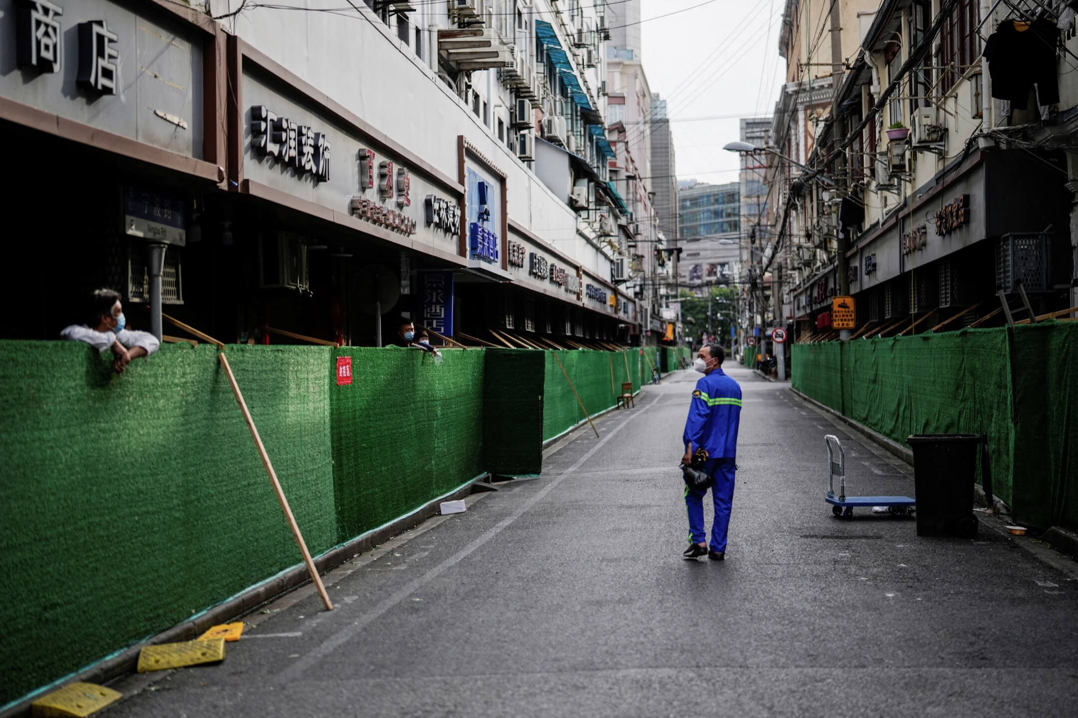 2022年5月18日，中国上海，一名清洁工人在围封的住宅区间走过，与被围封的居民对望。