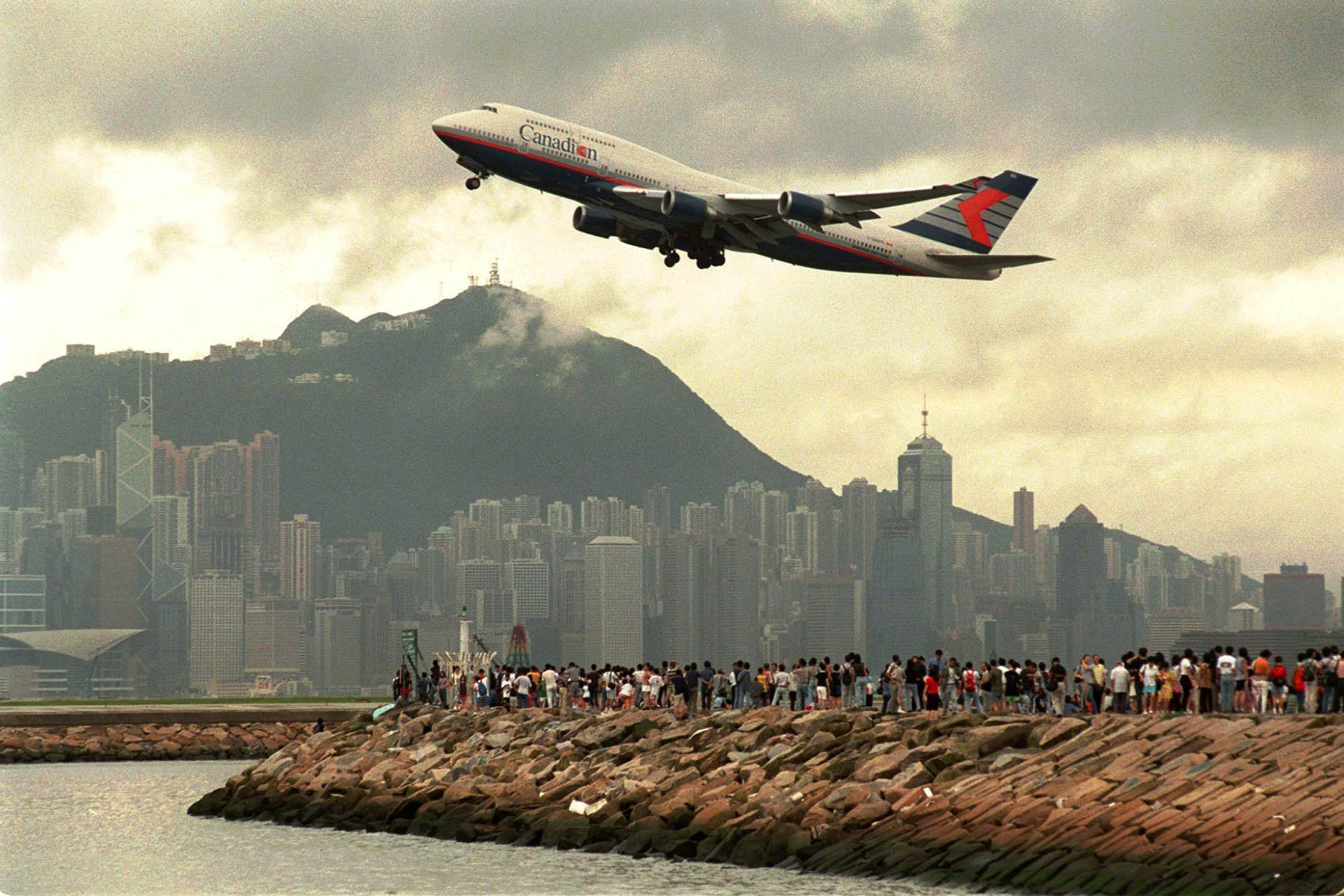 1998年7月5日，香港启德机场跑道旁边的海港，大批人群聚集在海堤上，观看最后一架飞机离开机场。