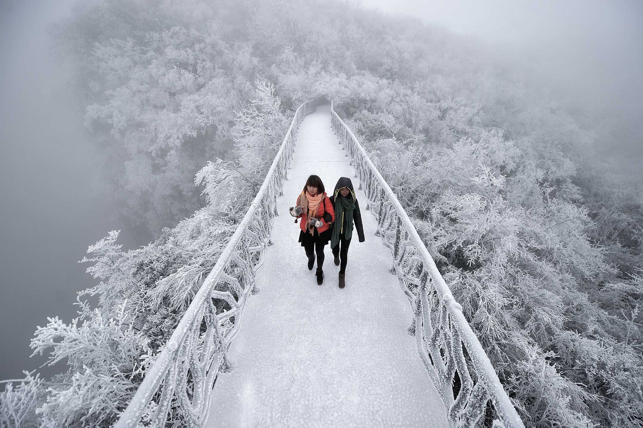 湖南张家界，二名女孩在一座被雪覆盖的桥上行走。