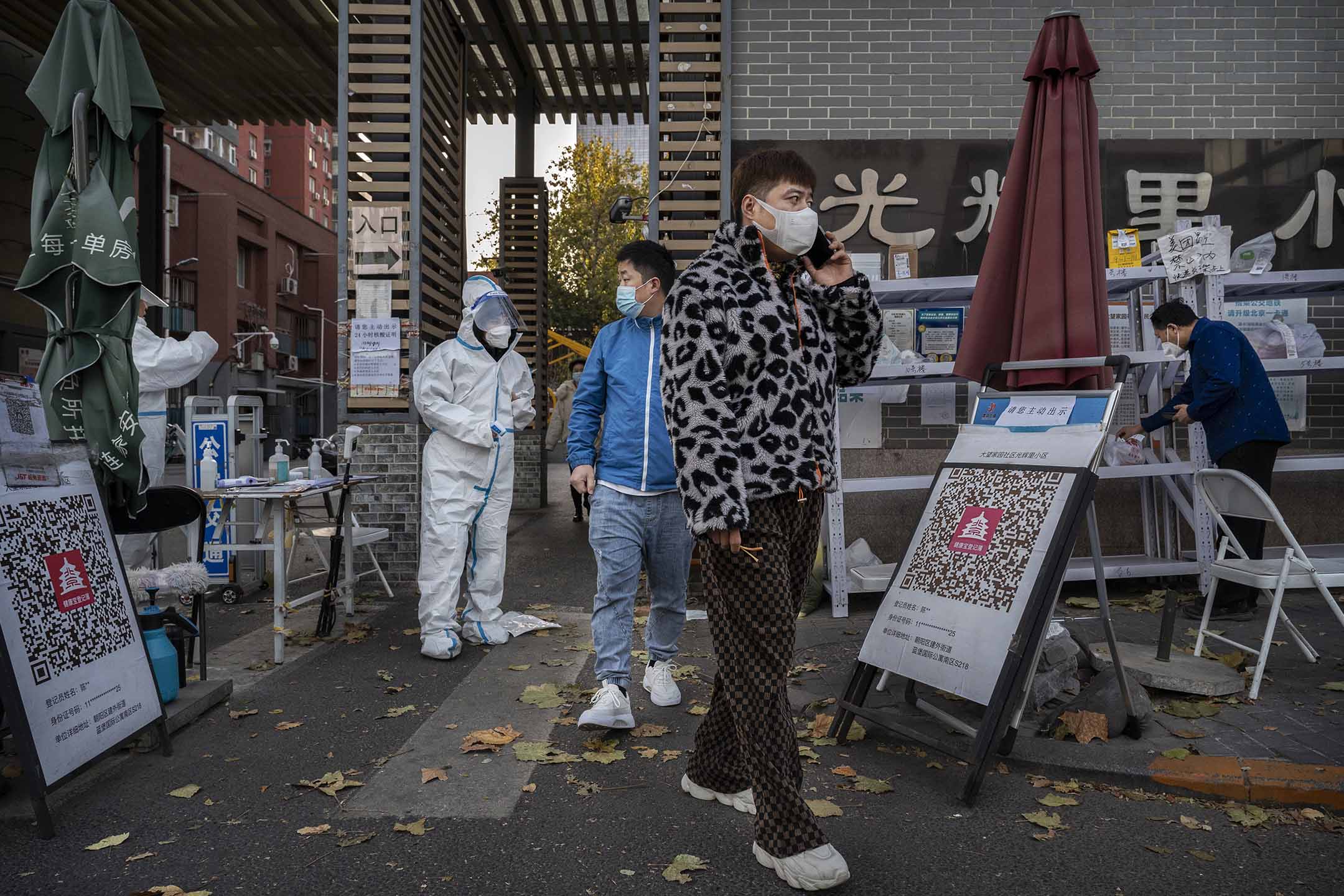 2022年11月25日，北京，一名防疫人员身穿防护服站岗，公寓大楼居民出来领取包裹。