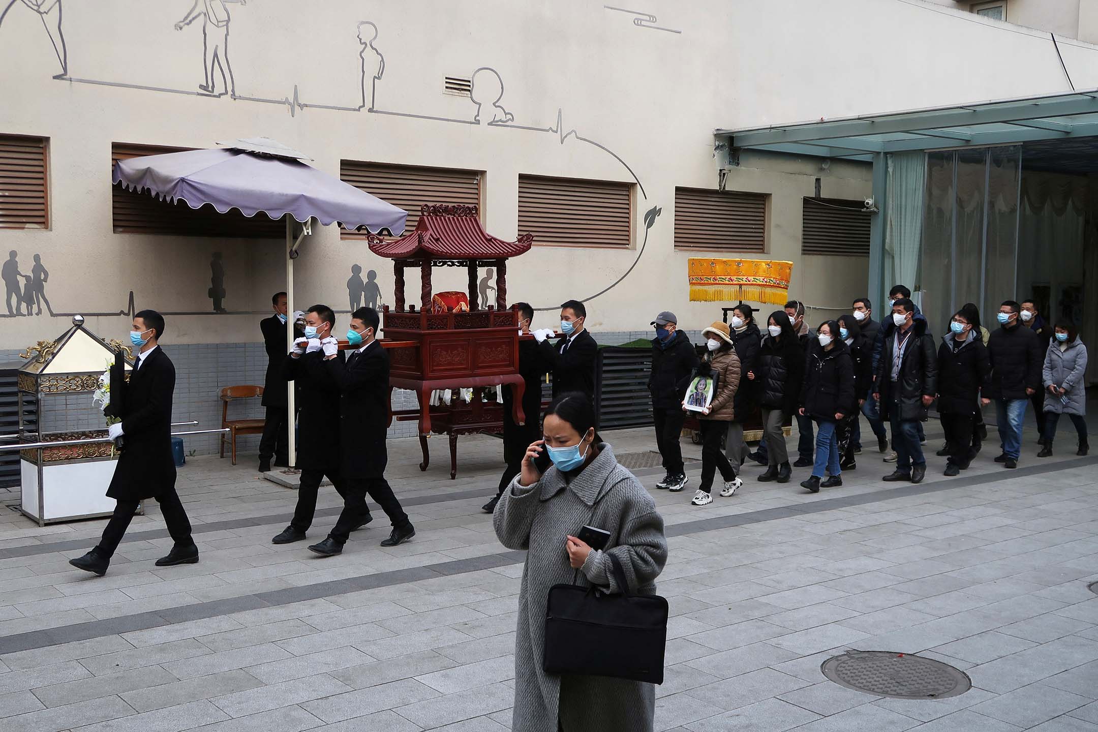 2022年12月28日，四川省成都，工作人员在火葬场外带著骨灰盒参加送葬队伍。