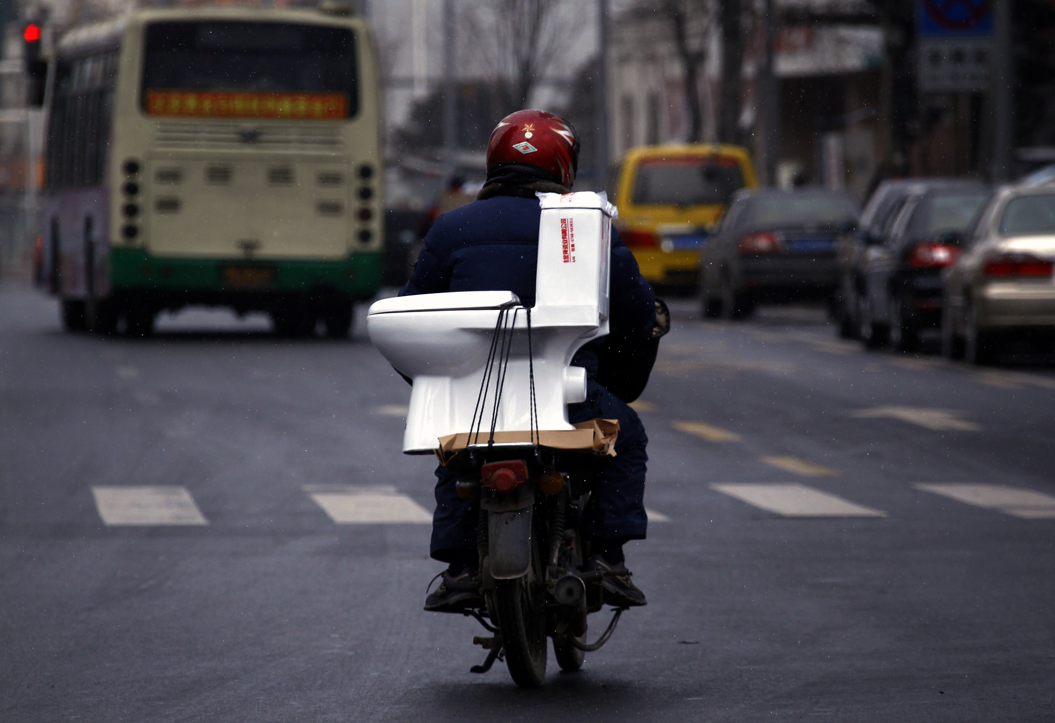 2012年2月7日，山東省煙台市，一名男子在街道上騎著一輛摩托車，一個馬桶綁在座椅後部。