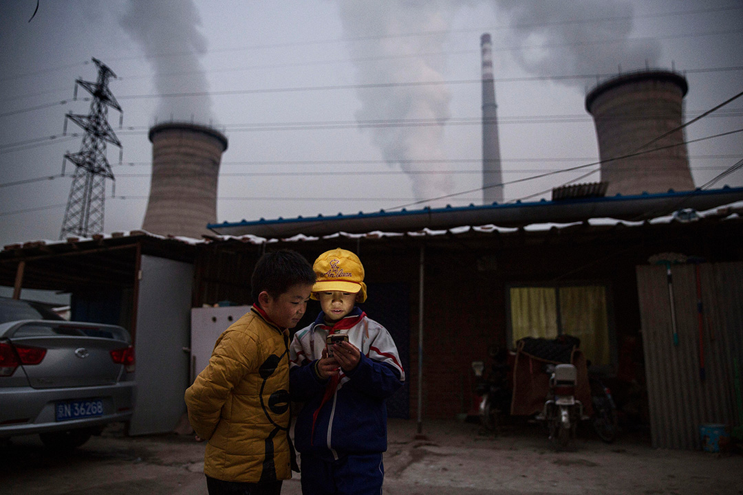 2015年11月27日， 中国北京，一对男孩在燃煤发电厂前使用智能手机。摄：Kevin Frayer/Getty Images