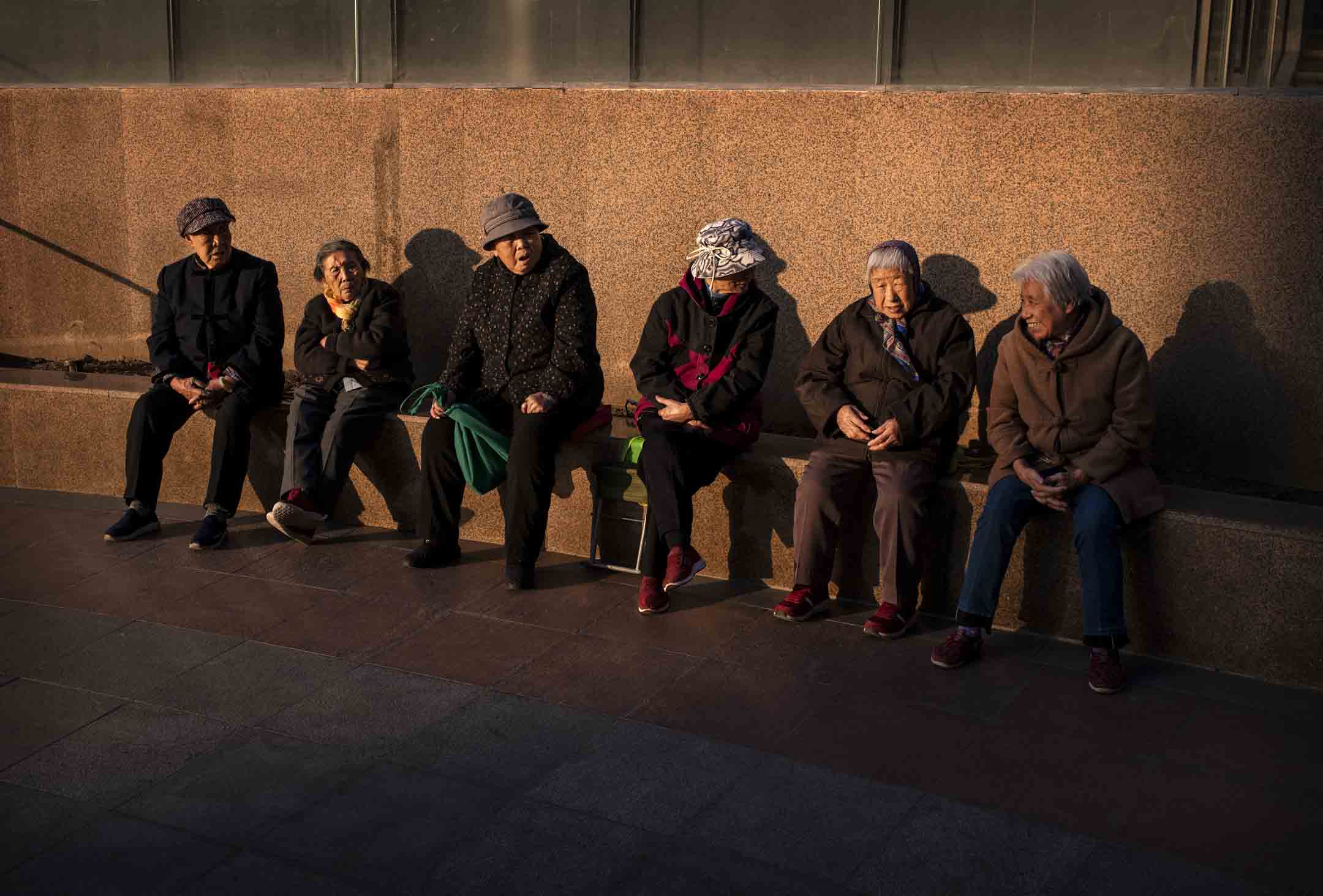 2019年11月8日，中国北京的一家购物中心外，长者在夕阳下聊天。摄：Kevin Frayer/Getty Images