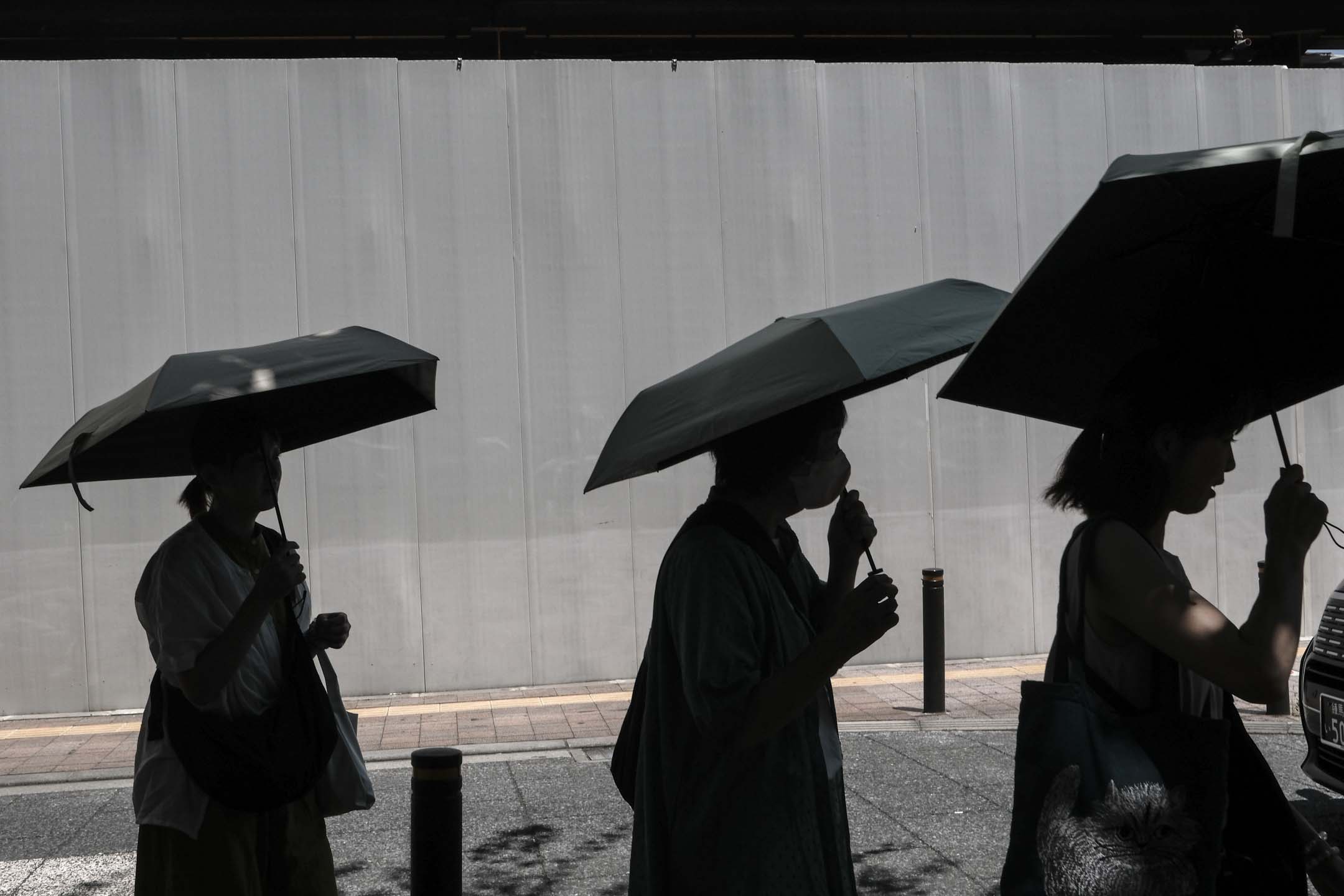 2023年7月10日，日本东京，行人在遮阳伞下躲避阳光。摄：Soichiro Koriyama/Bloomberg via Getty Images