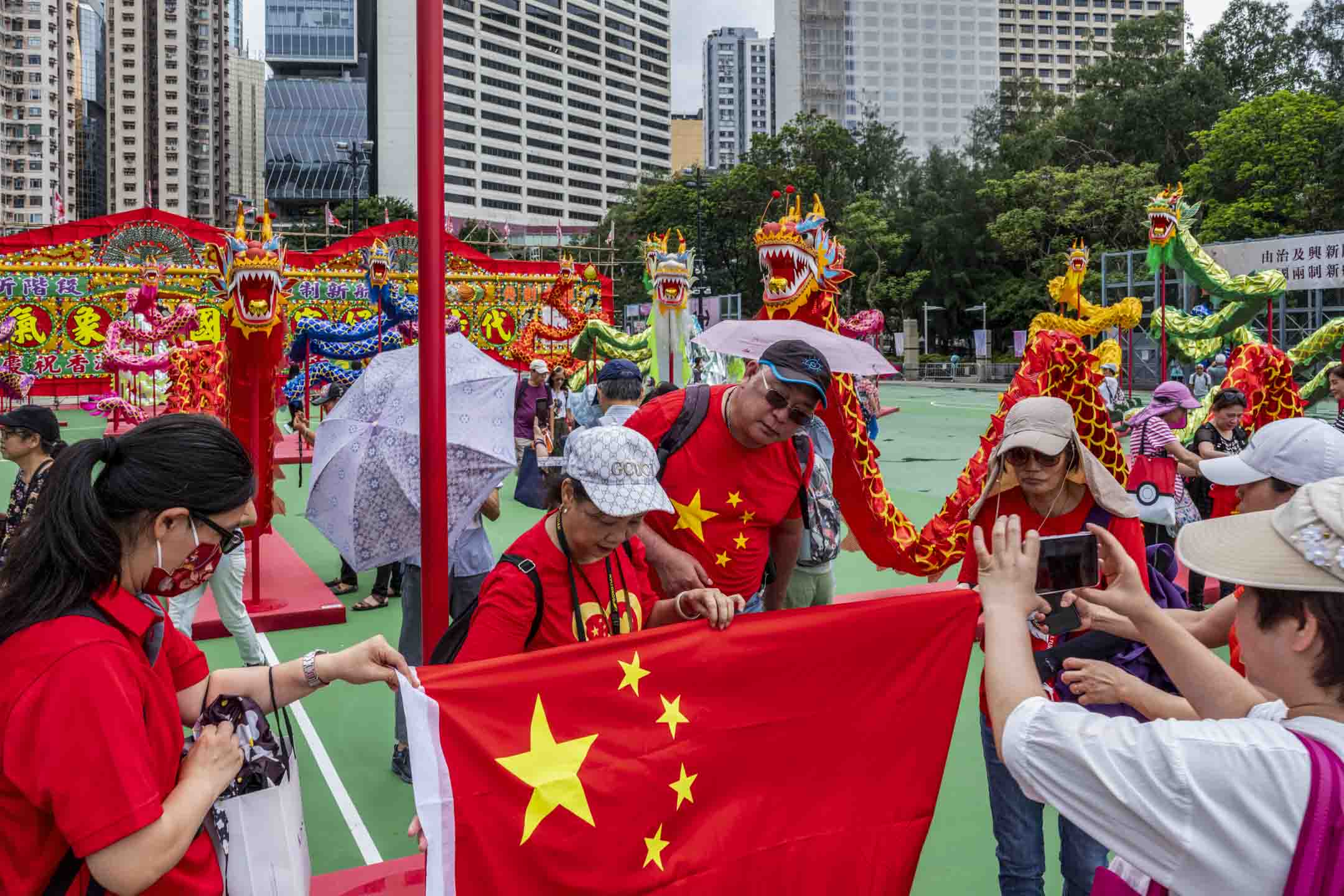 2023年6月30日，维园“庆祝香港回归祖国二十六周年”庆祝活动，现场有本地特色大型花牌配合26条传统舞龙，市民带同国旗拍照。摄：林振东/端传媒