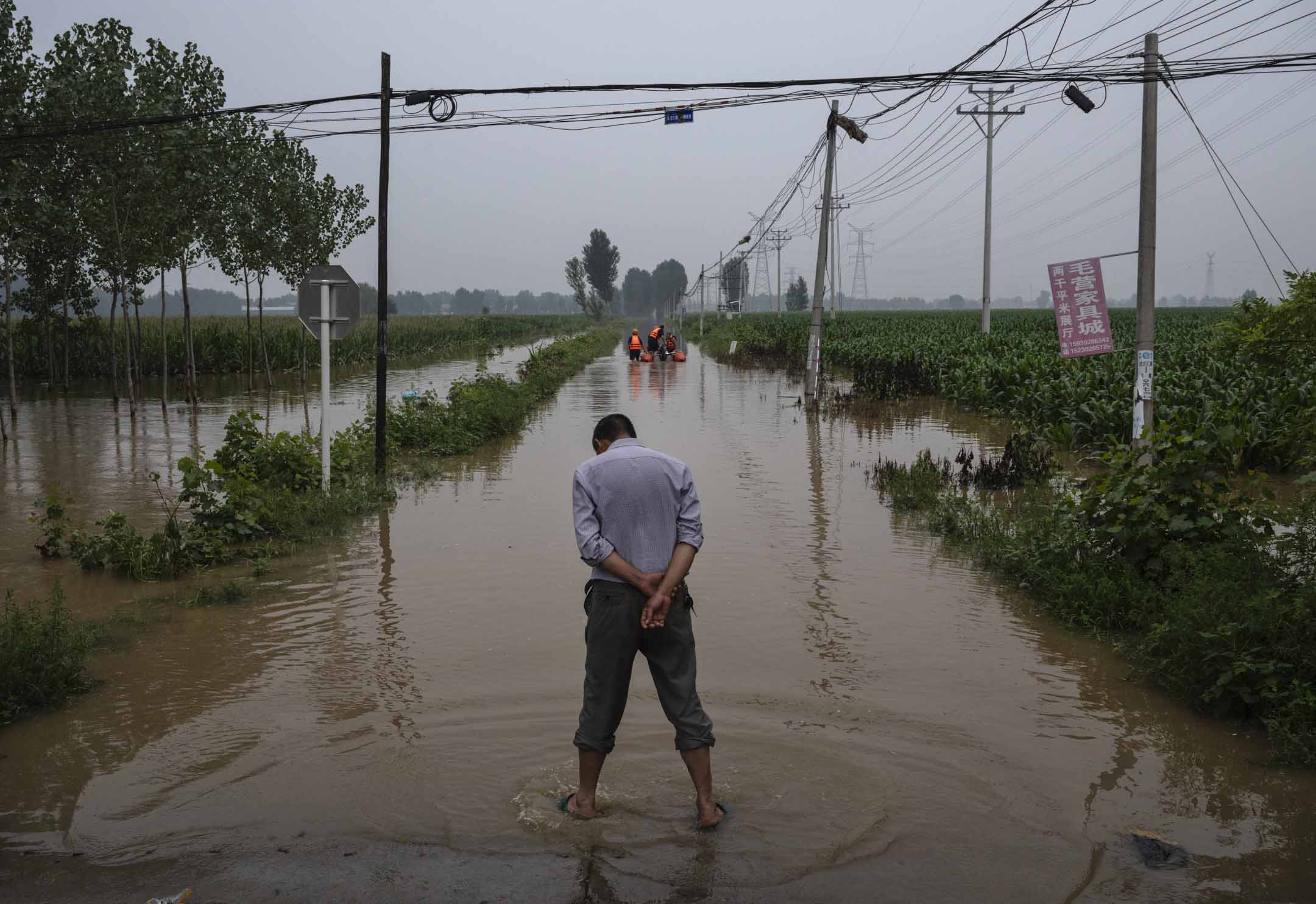 2023年8月3日，中国河北省涿州附近的一个被洪水淹没的地区，一名当地居民等待救援人员船只。摄：Kevin Frayer/Getty Images