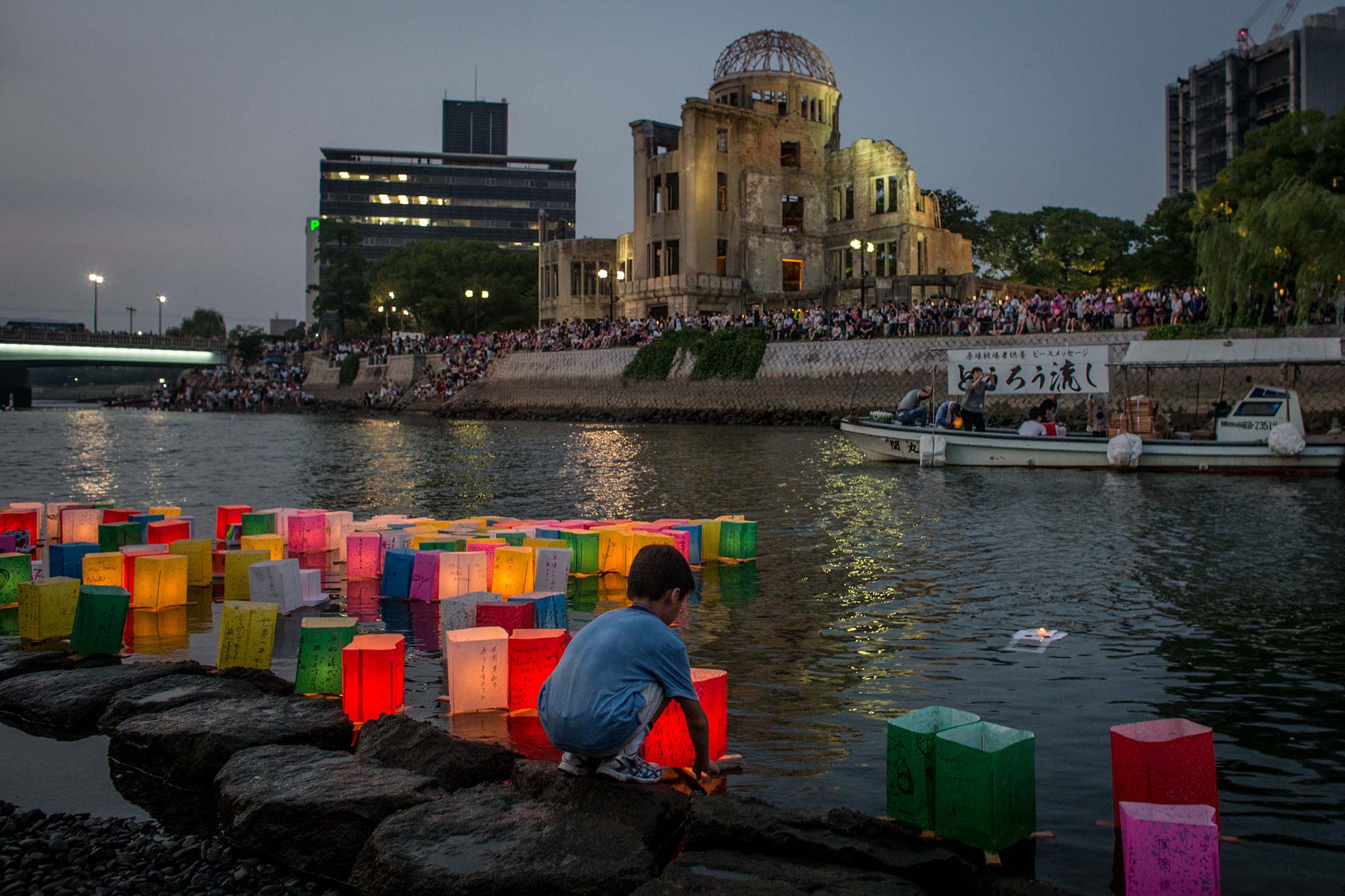 2015年8月6日，日本广岛，一名男孩在当年原子弹的爆炸现场，漂浮蜡烛点燃的纸灯笼，纪念当年的遇难者。摄：Chris McGrath/Getty Images