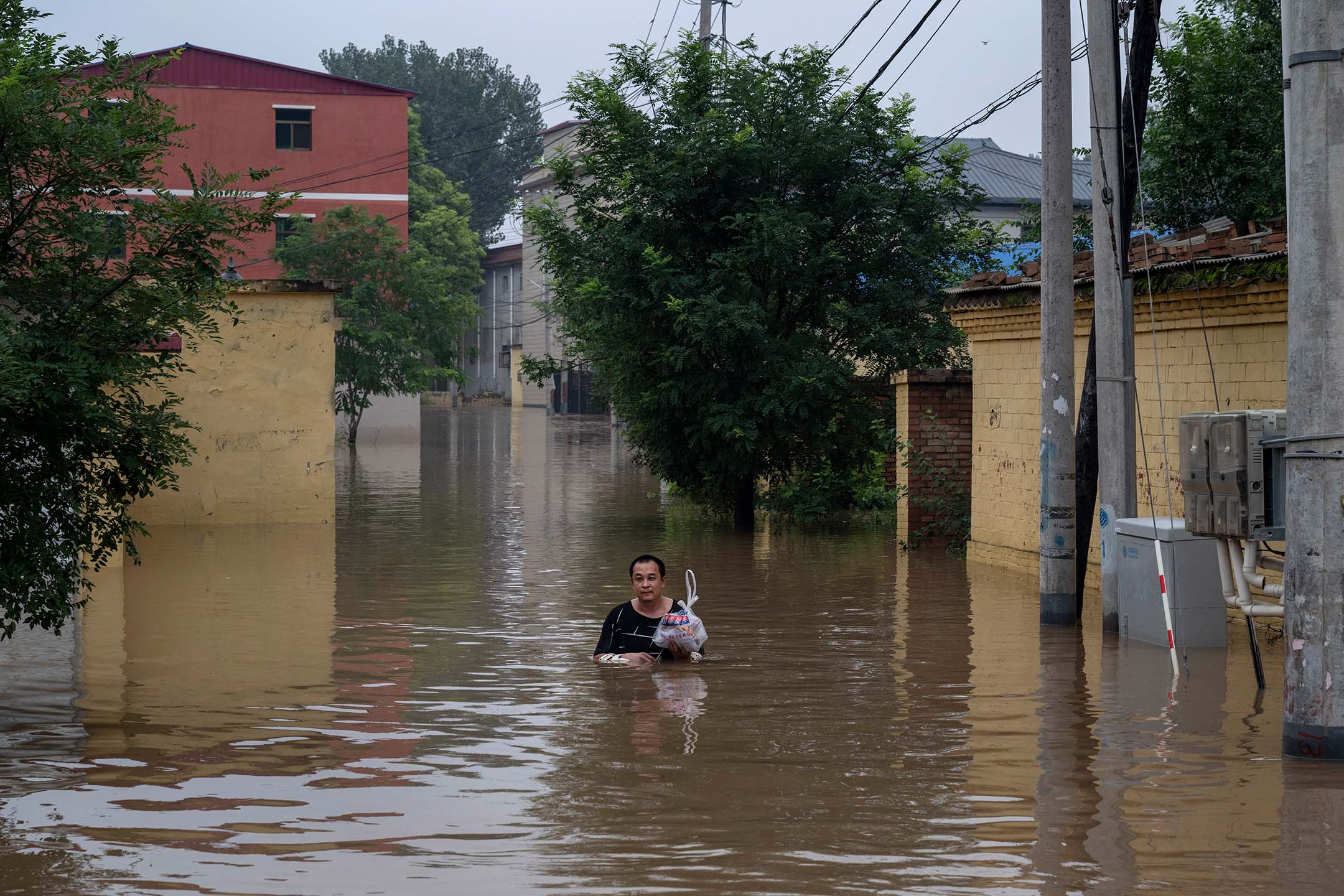 2023年8月3日，中国涿州，一名当地居民在水深及胸的洪水下，涉水走向一艘救援船。摄：Kevin Frayer/Getty Images