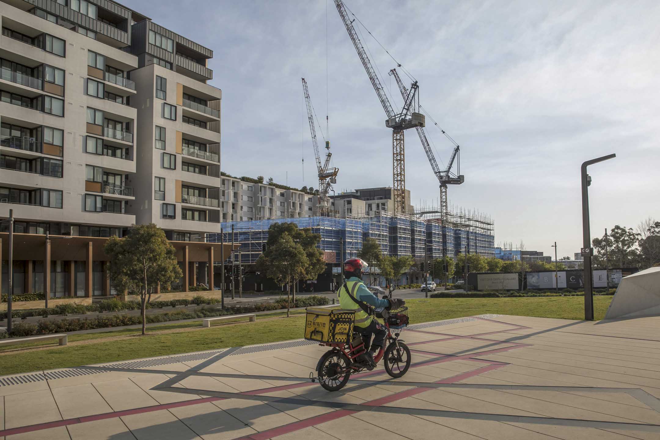 2023年9月11日，一名外卖送餐员骑著单车经过澳大利亚悉尼 Green Square 地区的高层住宅大楼。摄：Brent Lewin/Bloomberg via Getty Images