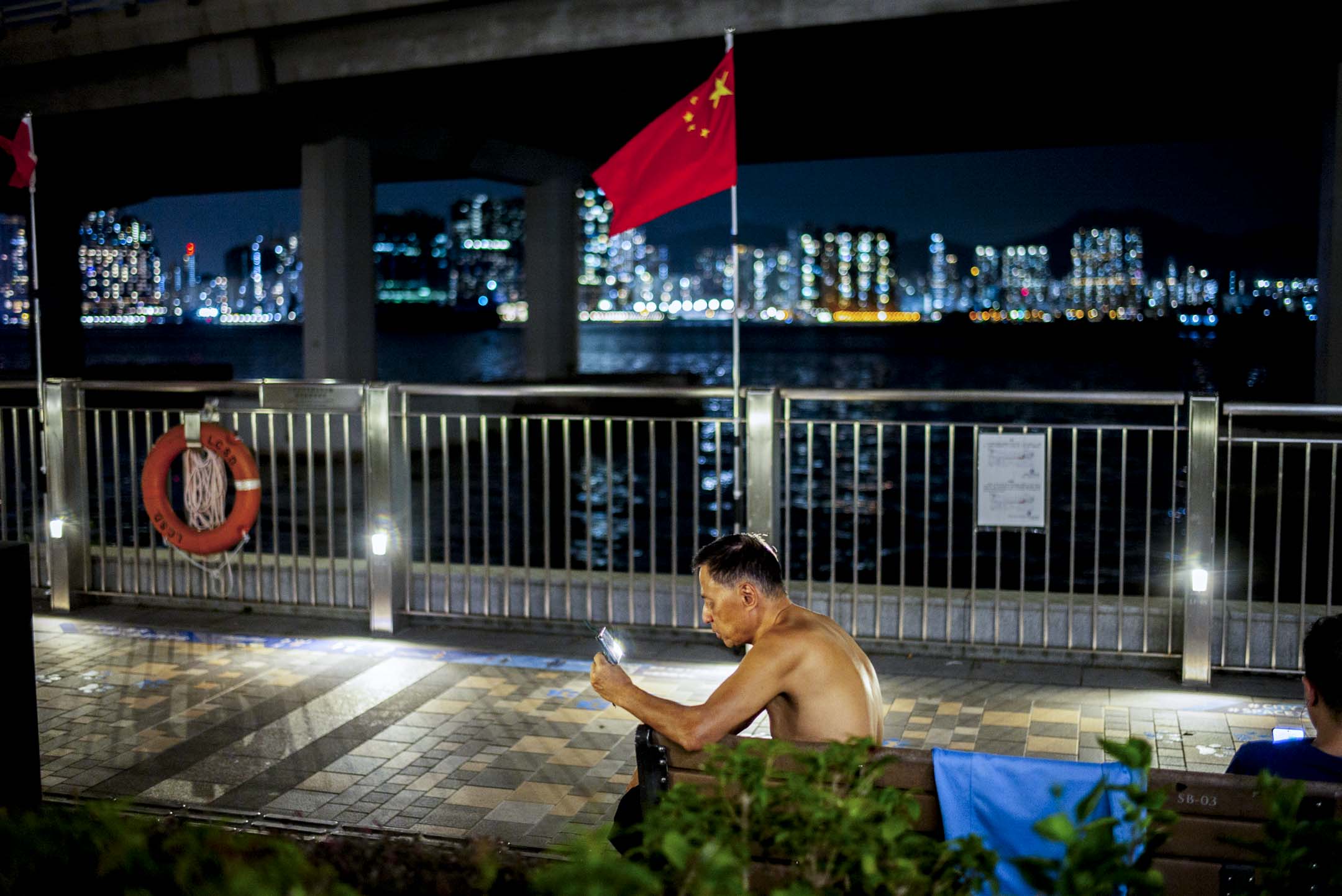 北角碼頭，一位脫去上衣的男士觀看手機。攝：林振東/端傳媒  