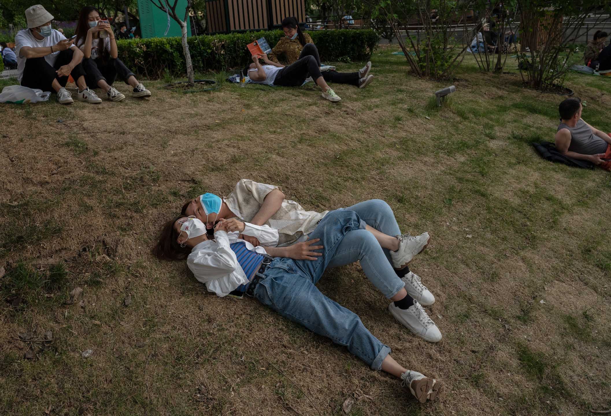 2022年5月15日，中国北京，一对情侣躺在公园草地上。摄：Kevin Frayer/Getty Images