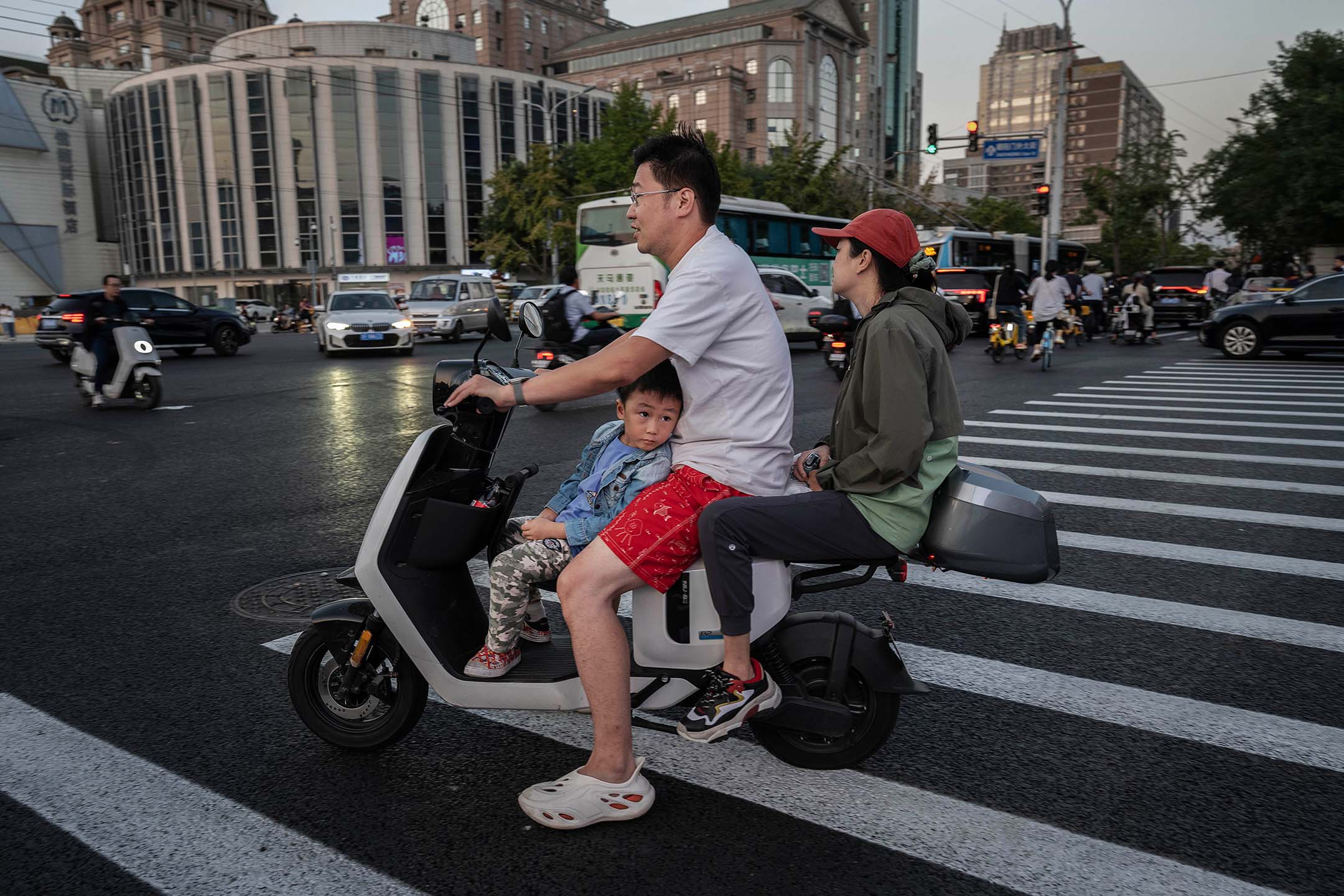 2023年9月13日，中國北京，一家人騎著摩托車在馬路旁邊等待。攝： Kevin Frayer/Getty Images