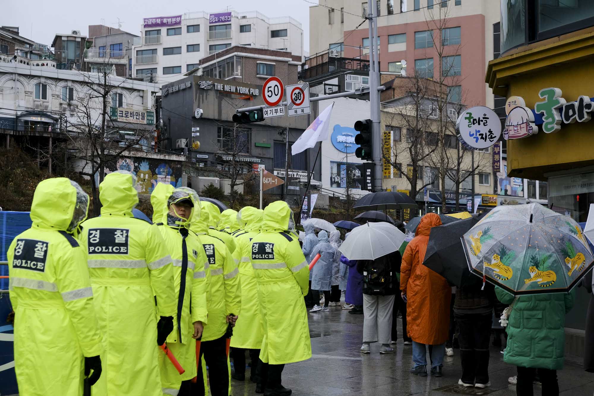 2023年12月14日，遗属游行到对岸的国会大楼，三十个身穿萤光背心的警员跟在家属旁边，形成一道警墙，阻隔他们与路上的车流。摄：余美霞/端传媒