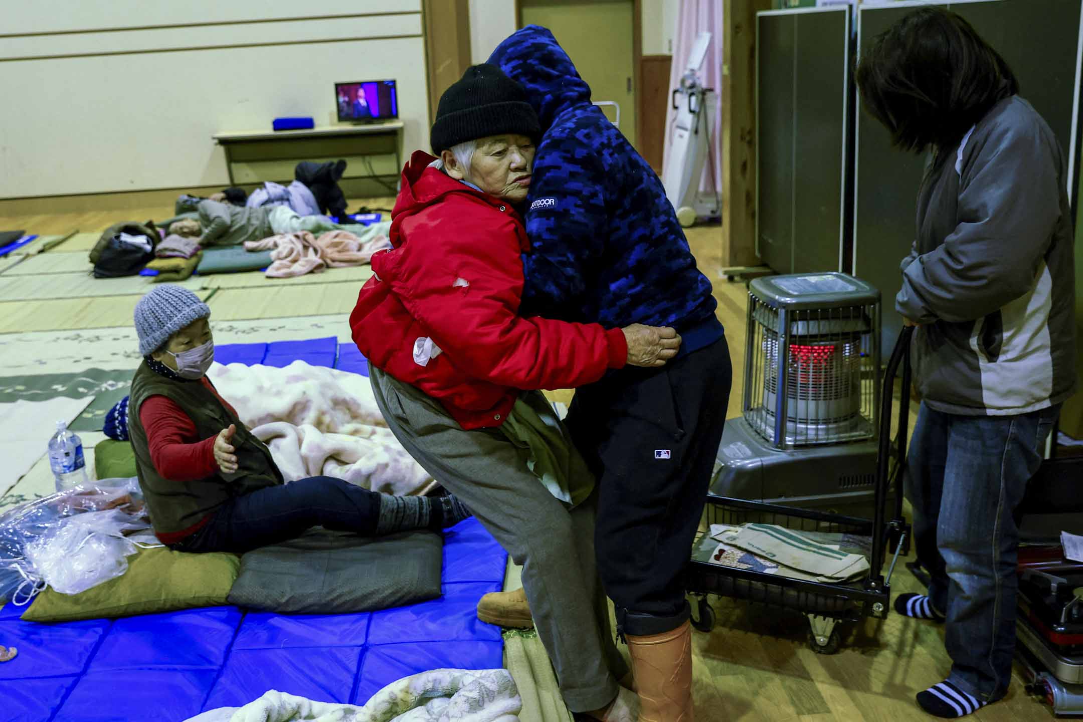 2024年1月2日，日本石川縣輪島，地震發生後，一名男子幫助他的母親躺在社區中心的床墊上，該社區中心已改建成疏散中心。攝：Kim Kyung-Hoon/Reuters/達志影像