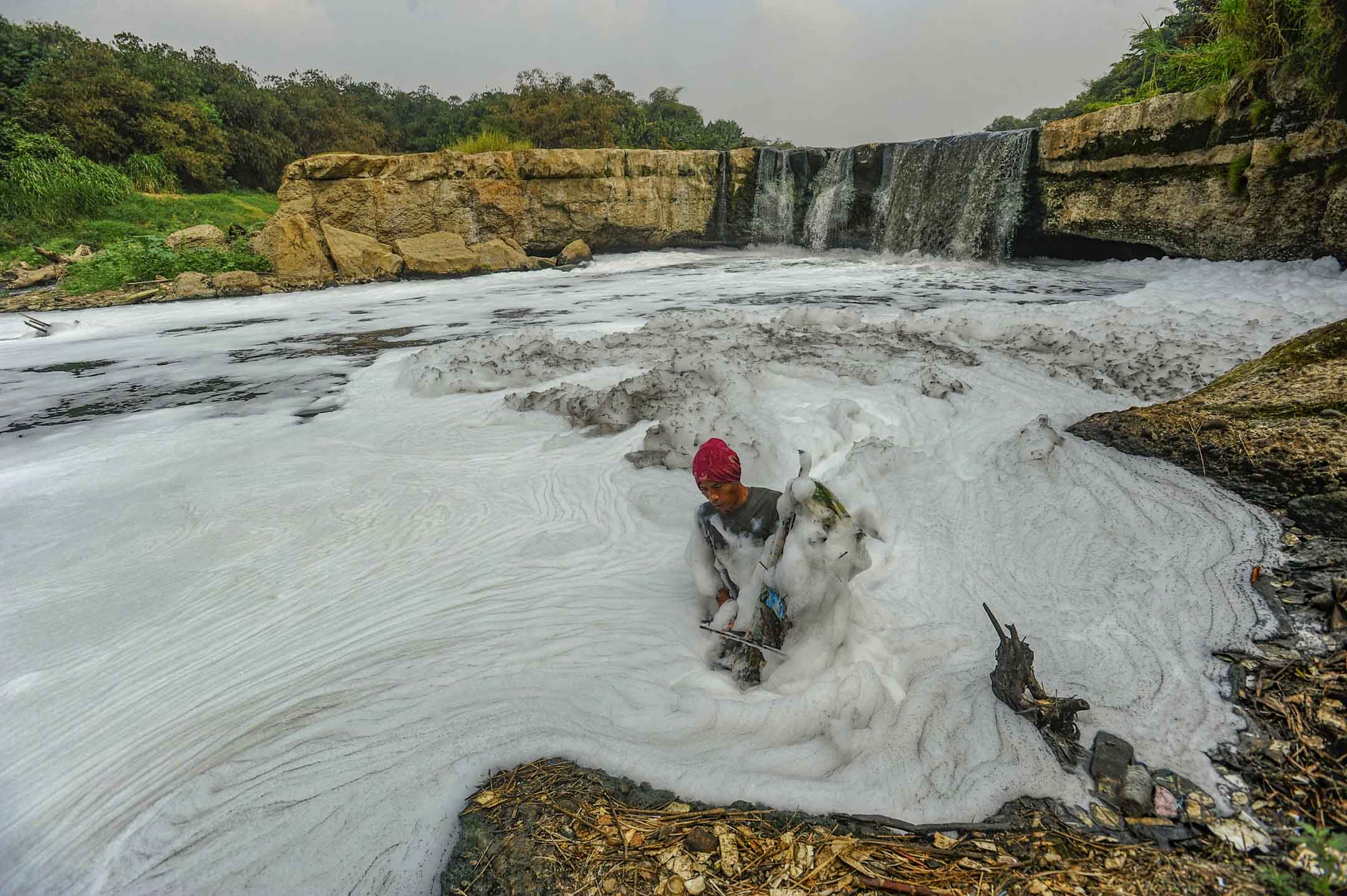 2023年8月27日，印尼 Curug Parigi，一名居民在Cileungsi 河中釣魚，那裡曾經是風景優美的瀑布。 水面上的濃稠泡沫，來自附近工業廢水。 攝： Arie Basuki