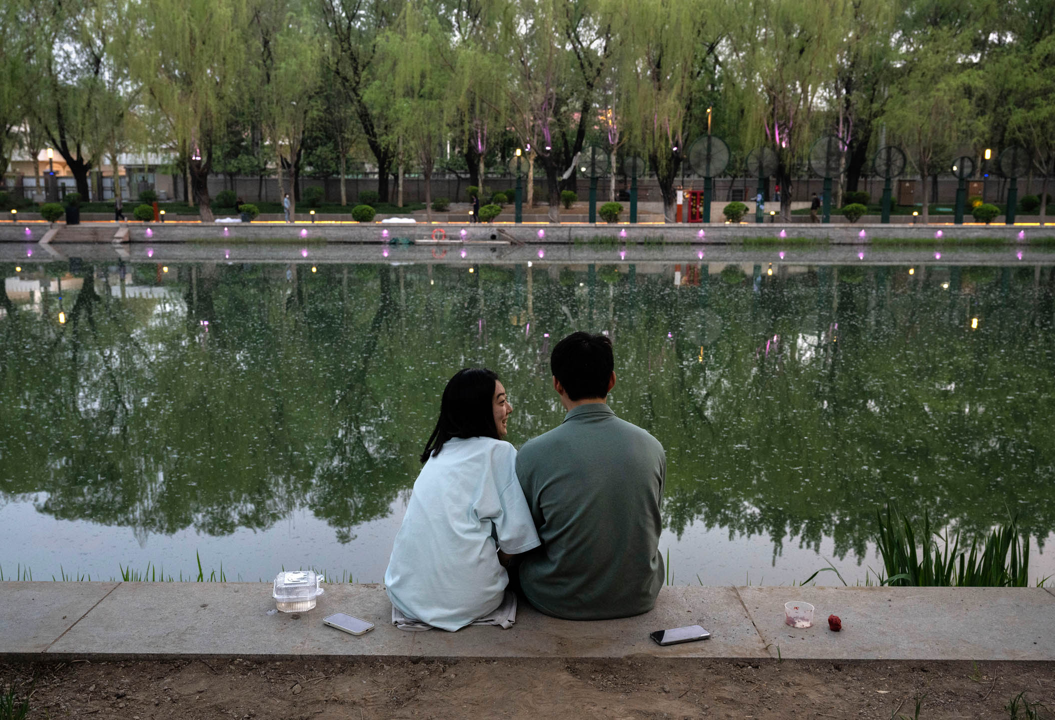 2024年4月12日，中国北京，一对情侣坐在河边钓鱼。摄：Kevin Frayer/Getty Images