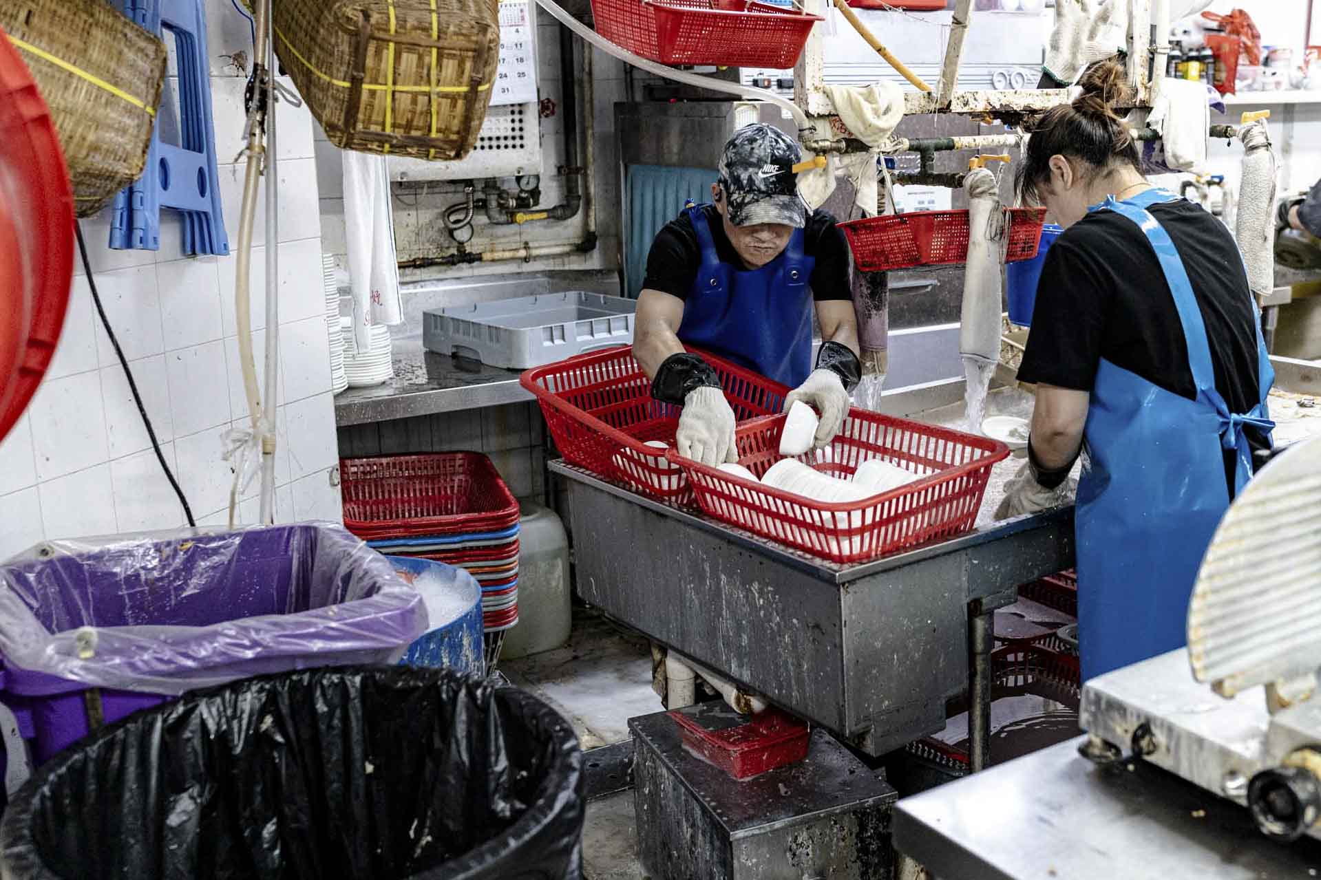 新光宴會廳的員工正在廚房洗碗，以及將廚餘放在紫色廚餘桶內。攝：Ryan Lai/端傳媒