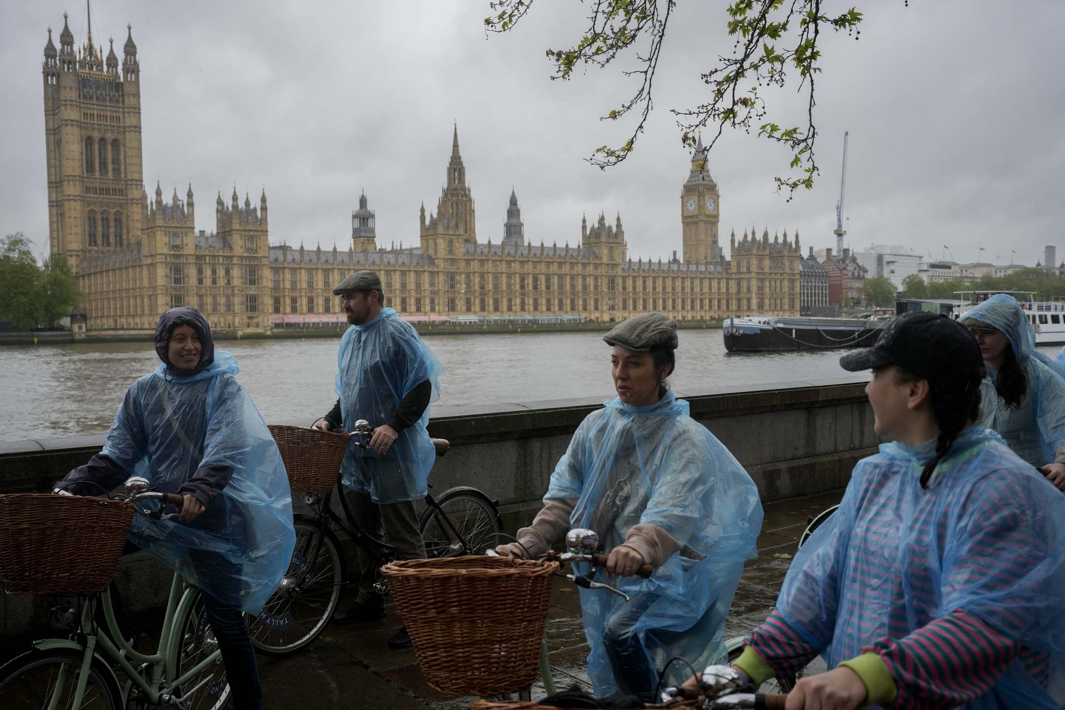 2024年5月3日，英国伦敦，游人穿著潮湿的塑胶雨伞骑自行车游览议会大厦。摄：Kin Cheung/AP/达志影像