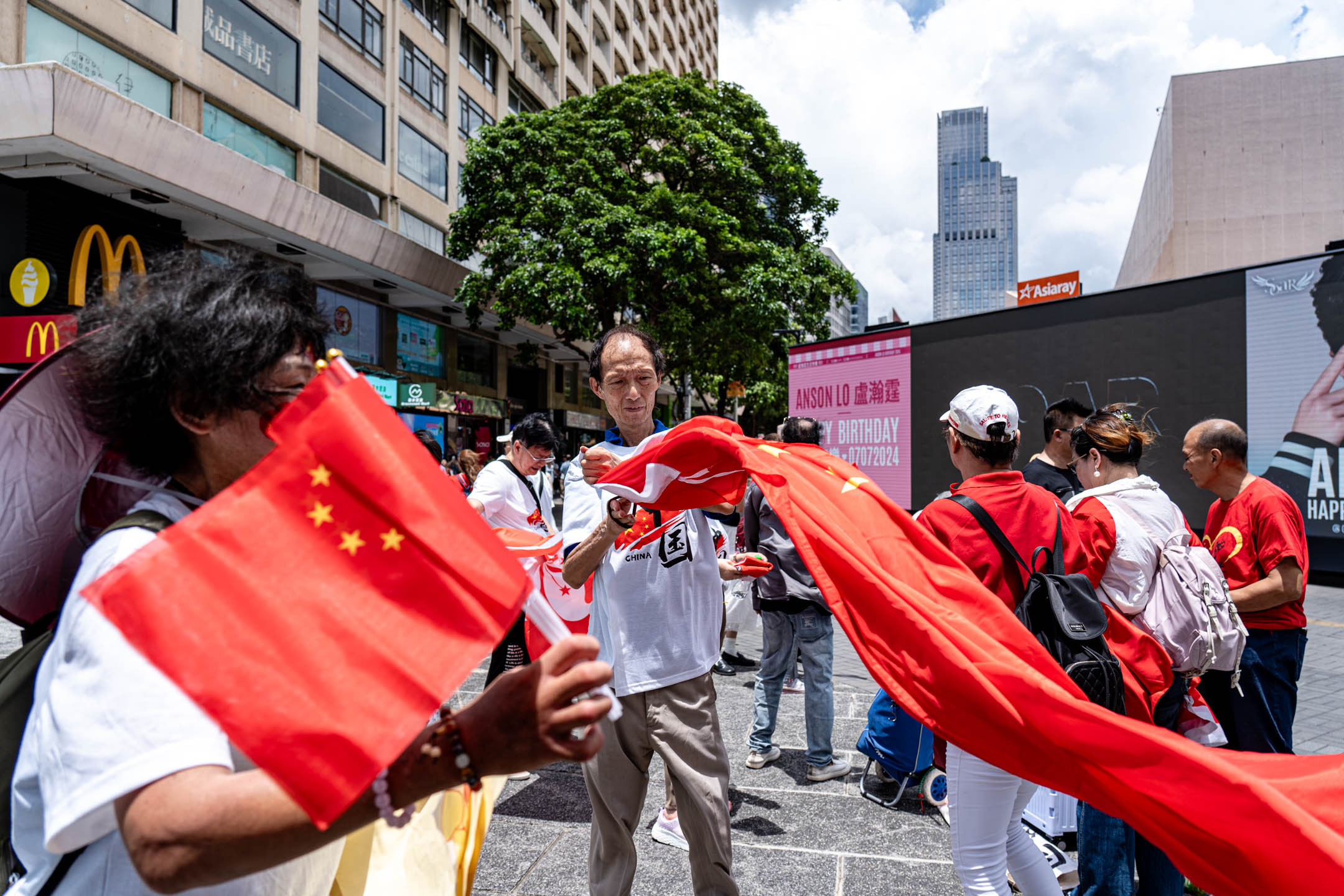 2024年7月1日，有市民在尖沙咀天星码头外挥动国旗与区旗，庆祝回归27周年。摄：Ryan Lai/端传媒