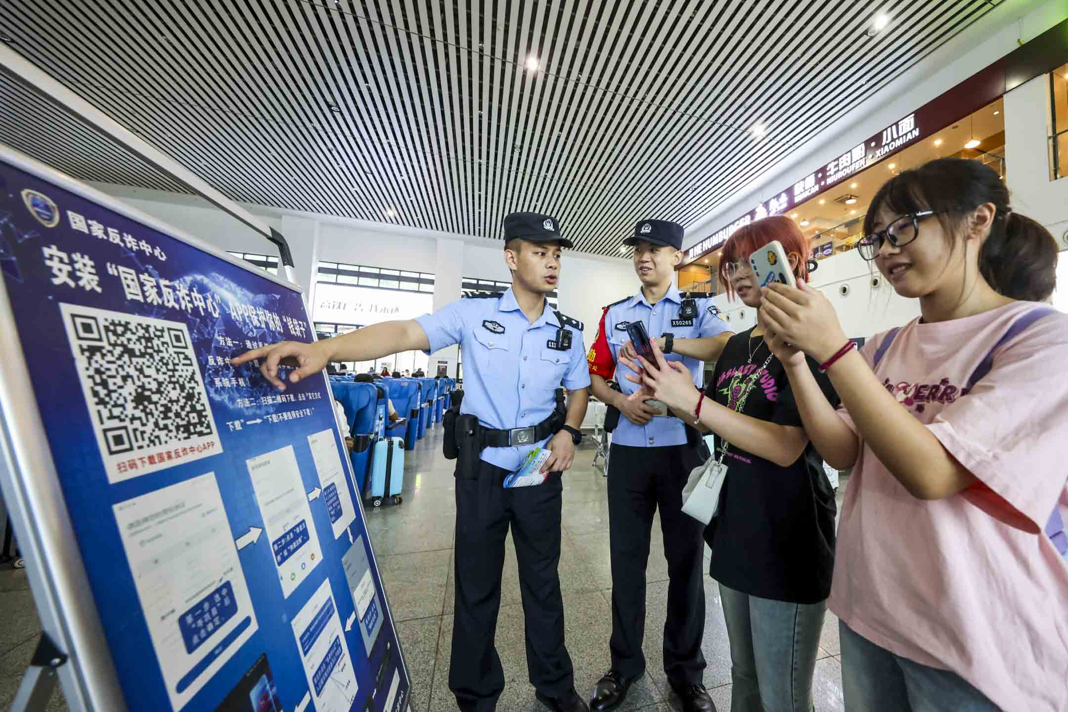 2023年8月24日，中国贵州，铁路警察引导乘客下载“反诈APP”。摄：CFOTO/Future Publishing via Getty Images