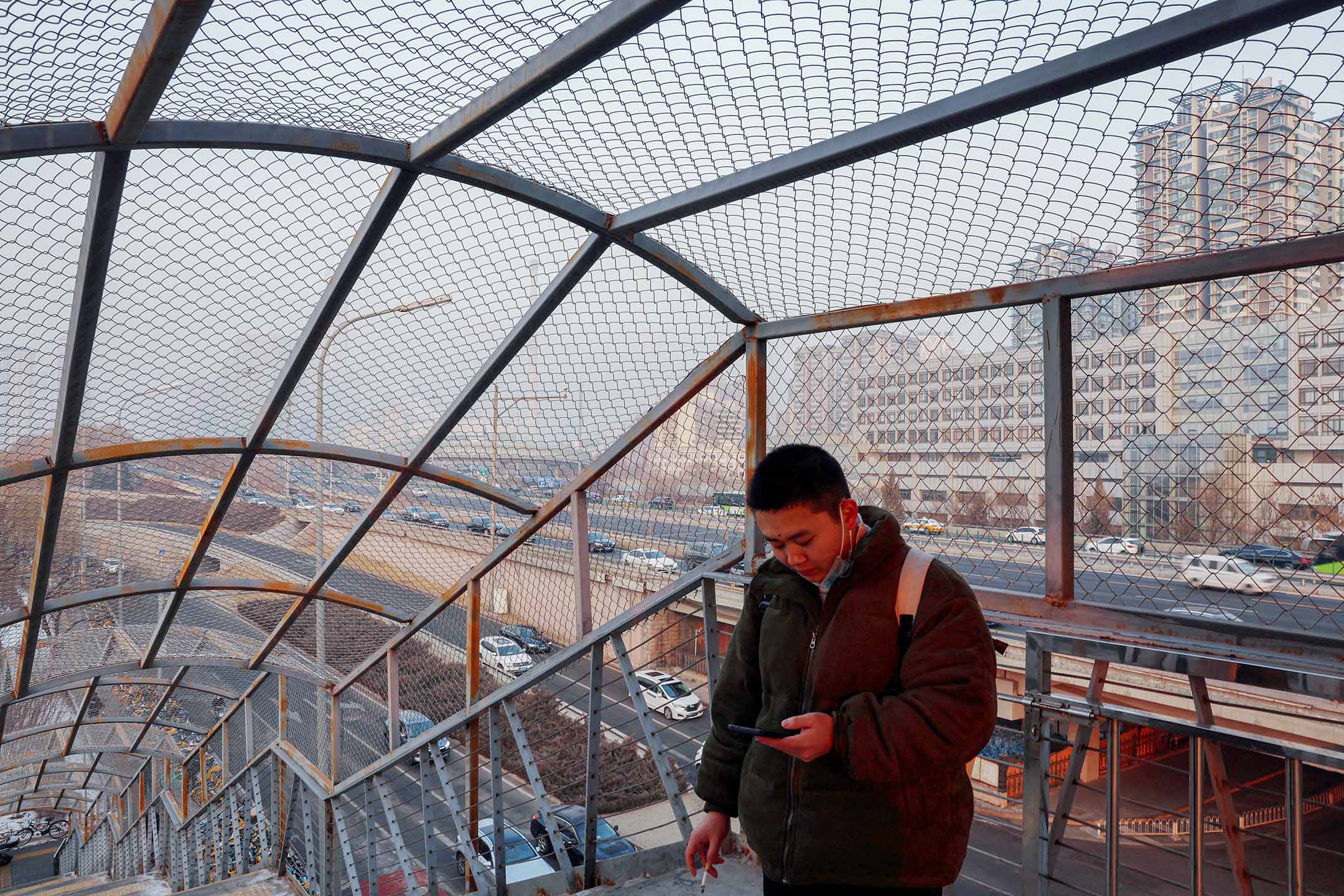 2024年1月12日，北京，一名男子在人行天桥上一边抽烟一边看手机。摄：Florence Lo/Reuters/达志影像