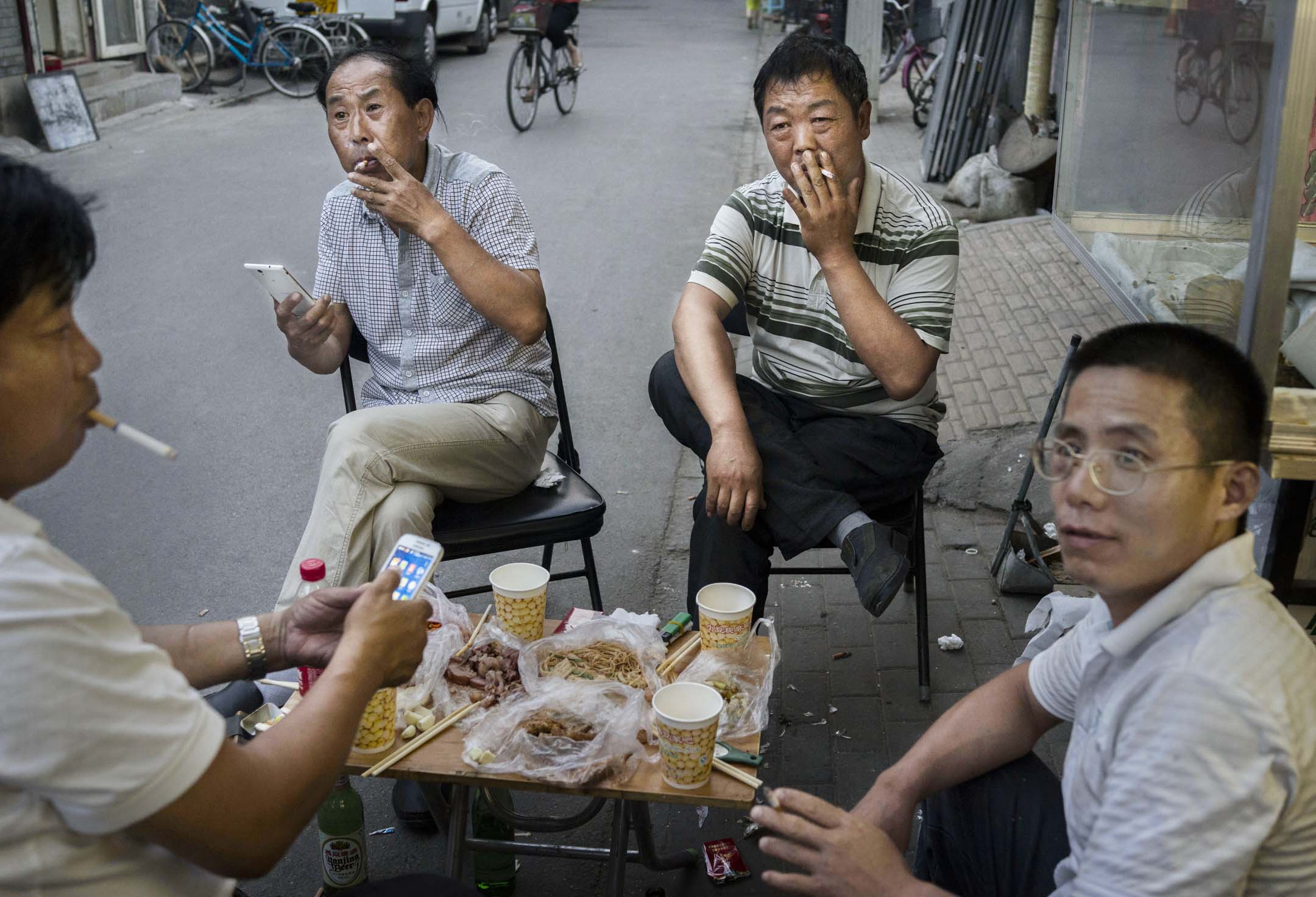 中國北京的男士在街上吃飯時一起抽煙。攝：Kevin Frayer/Getty Images