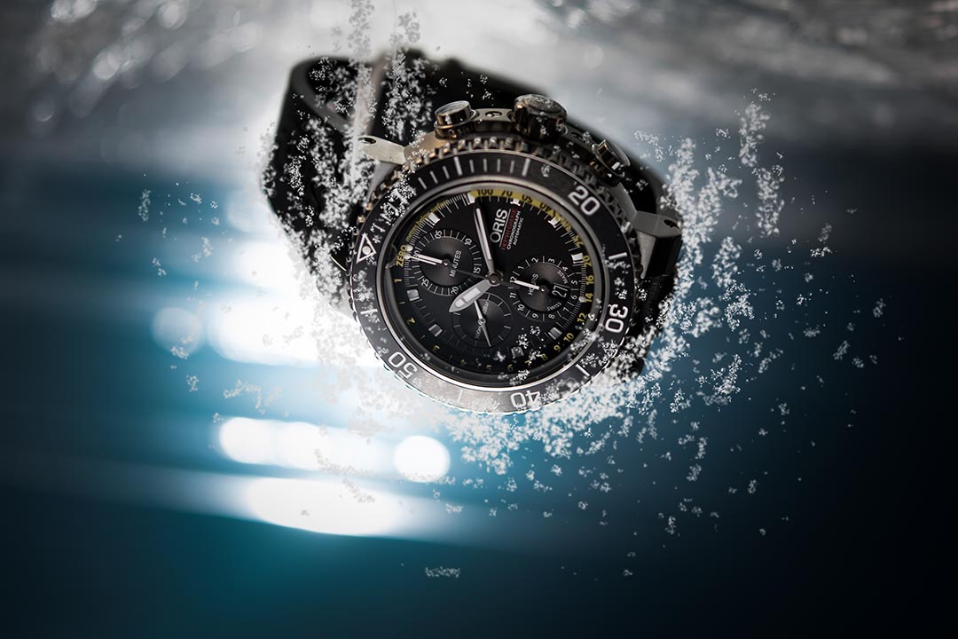 Oris Aquis Depth Chronograph ： 
12 时位置设有 1 个小孔，并在蓝宝石水晶玻璃外缘嵌入一条小管，潜水员下潜时，管道内的空气压缩让水可通过小孔进入管道。管道中的色彩变异与面盘上的黄色刻度相对应，潜水员便可清楚知道深度读数。摄：Lit Ma/端传媒