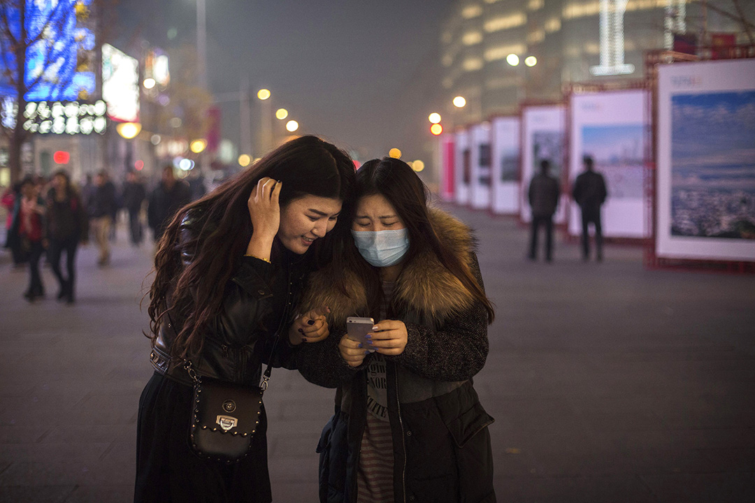 两位女士 在北京街头低头看手机上的信息。摄：Kevin Frayer/GETTY